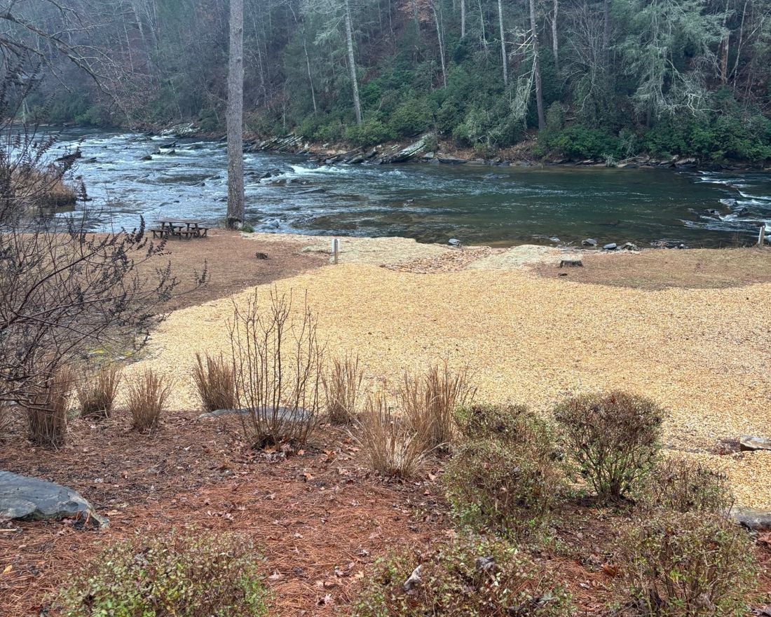 Riverbank in Gilmer County where vegetation has been removed and the ground covered in gravel down to the water